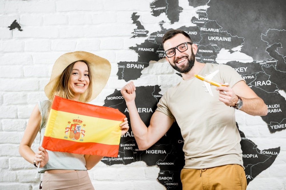 Pareja de jóvenes felices con una bandera de España y un avión de juguete, listos para estudiar y trabajar en España.