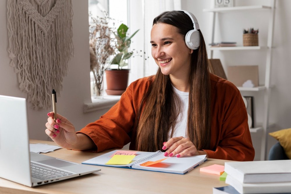 Joven estudiante con auriculares participando en una clase virtual desde casa, tomando notas en su cuaderno mientras cursa uno de los posgrados en España de forma remota.